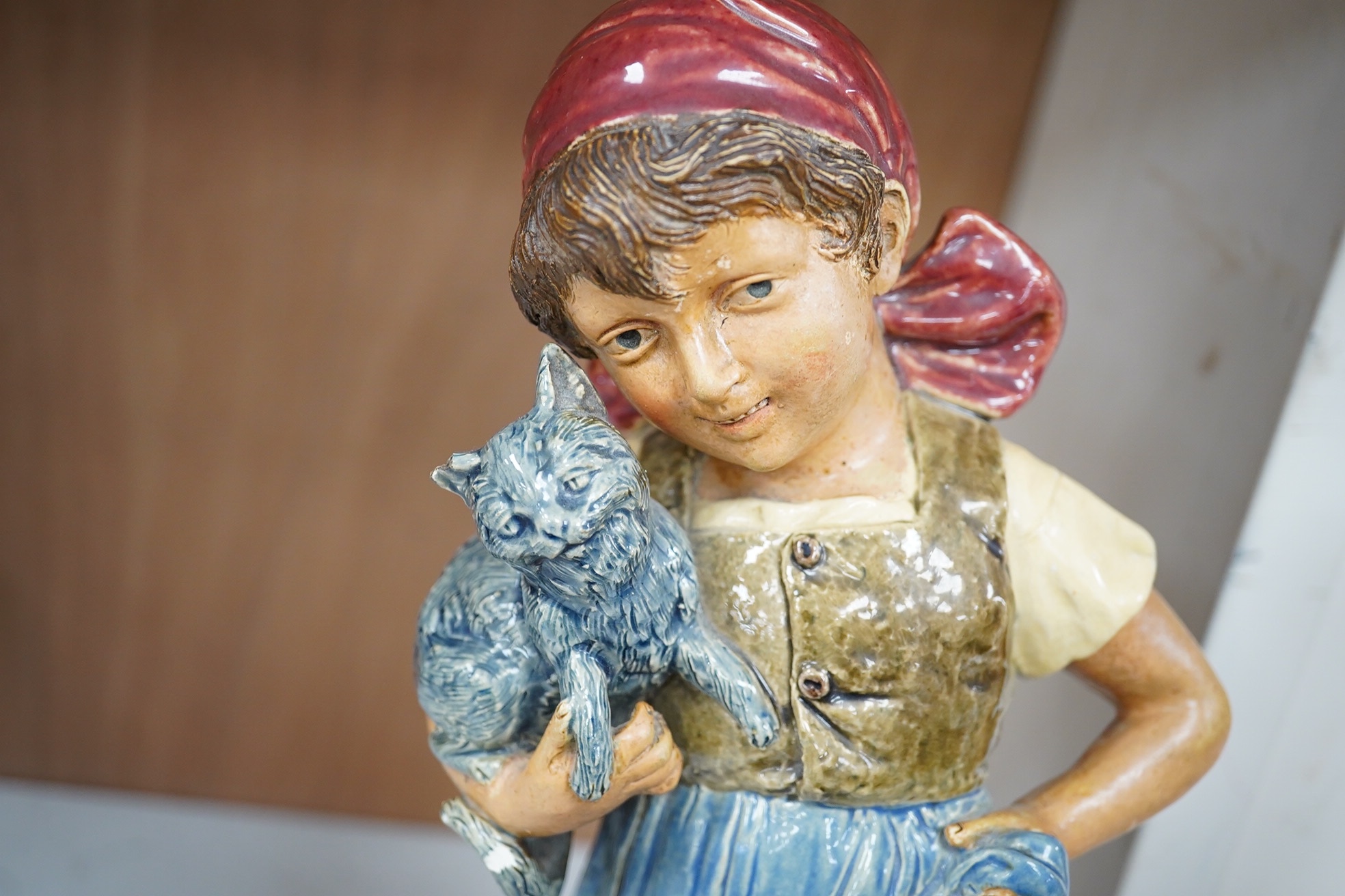 A pair of Austrian majolica figures of children, one holding a cat, the other a parrot, together with a similar smaller figure, tallest 37.5cm high (3). Condition - fair